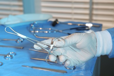 Photo of Doctor holding medical clamps near table with different surgical instruments indoors, closeup