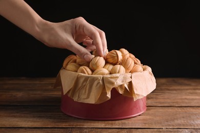 Photo of Woman taking walnut shaped cookie with boiled condensed milk from box at wooden table, closeup