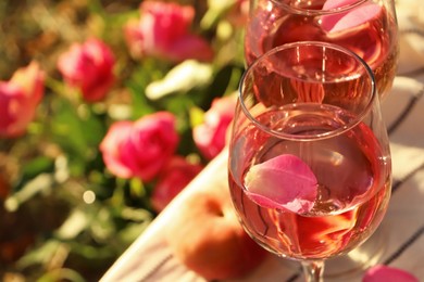 Photo of Glasses of delicious rose wine with petals outside, closeup. Space for text