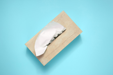 Photo of Wooden holder with paper tissues on light blue background, top view