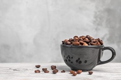 Photo of Cup with roasted coffee beans on wooden table