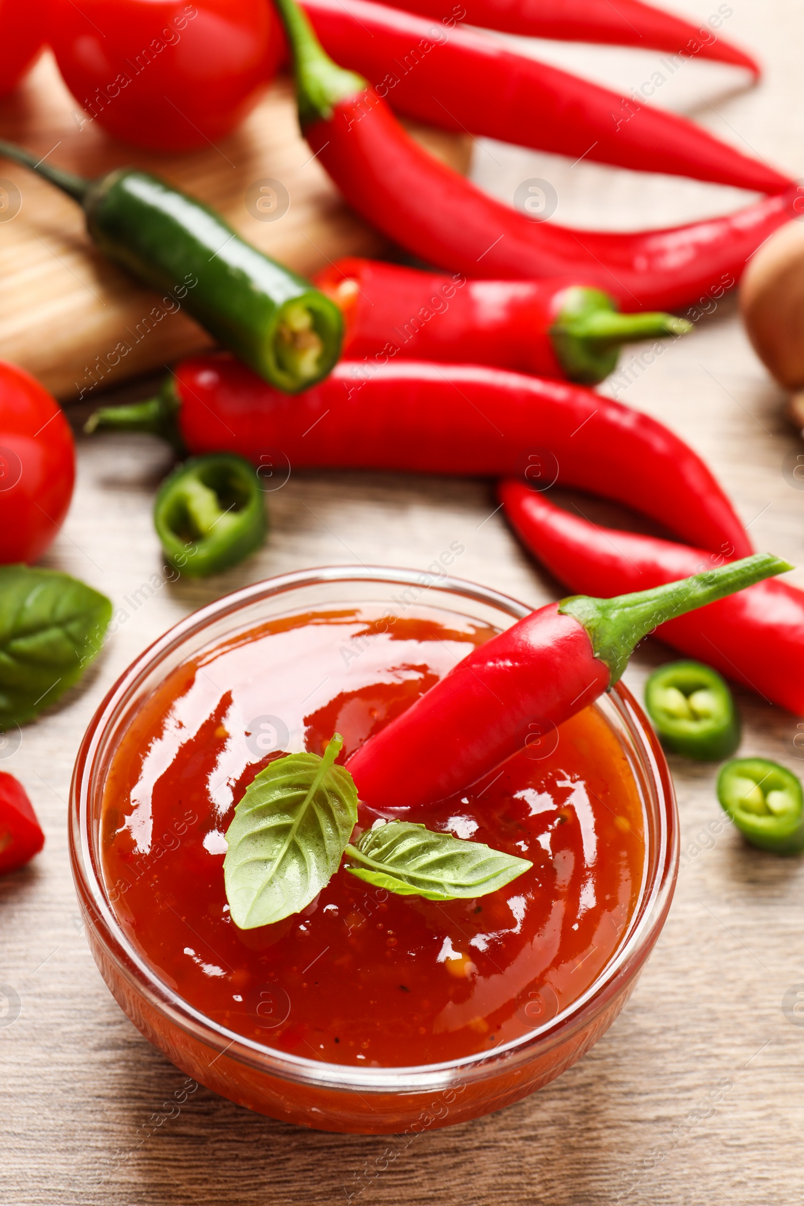 Photo of Spicy chili sauce with basil on wooden table