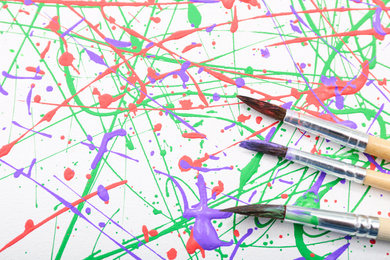 Photo of Brushes on canvas with colorful paint splashes, top view. Art and creativity