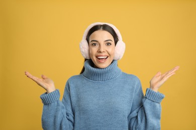 Photo of Beautiful young woman wearing earmuffs on yellow background