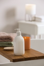 Tray with bottle of bubble bath, towels and candle on tub in bathroom