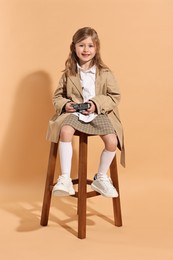 Photo of Fashion concept. Stylish girl with vintage camera on pale orange background
