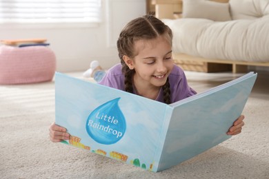 Photo of Cute little girl reading book on floor at home