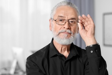 Photo of Portrait of handsome senior man in black shirt and eyeglasses at home