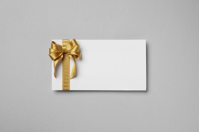 Photo of Blank gift card with golden bow on light gray background, top view