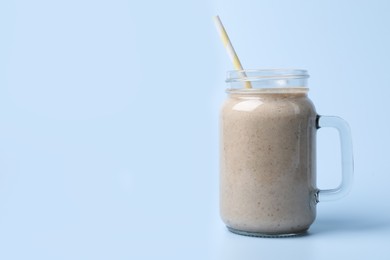 Photo of Mason jar with delicious fruit smoothie on light blue background. Space for text