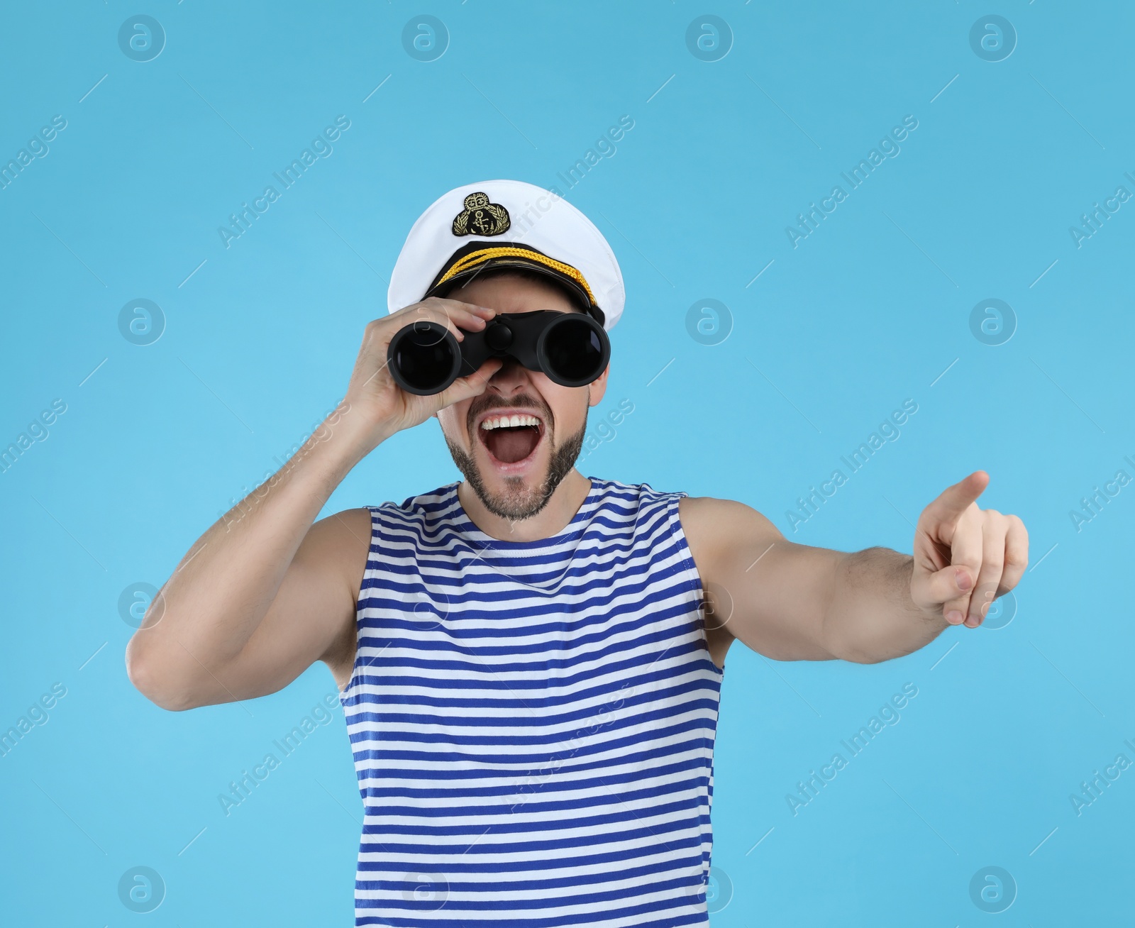 Photo of Sailor looking through binoculars and pointing on light blue background