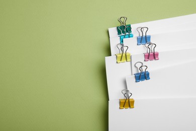 Photo of Sheets of paper with clips on light green background, top view. Space for text
