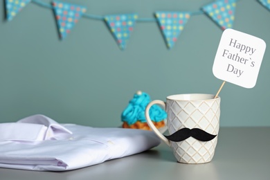 Photo of Cup with mustache, cake and shirt on table. Father's day celebration