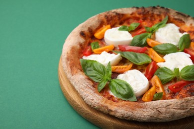 Photo of Delicious pizza with burrata cheese, tomatoes and basil on green background, closeup. Space for text