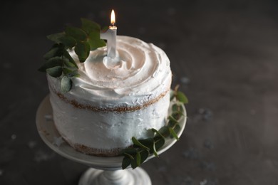Photo of Tasty Birthday cake with burning candle and eucalyptus branches on grey table, closeup. Space for text