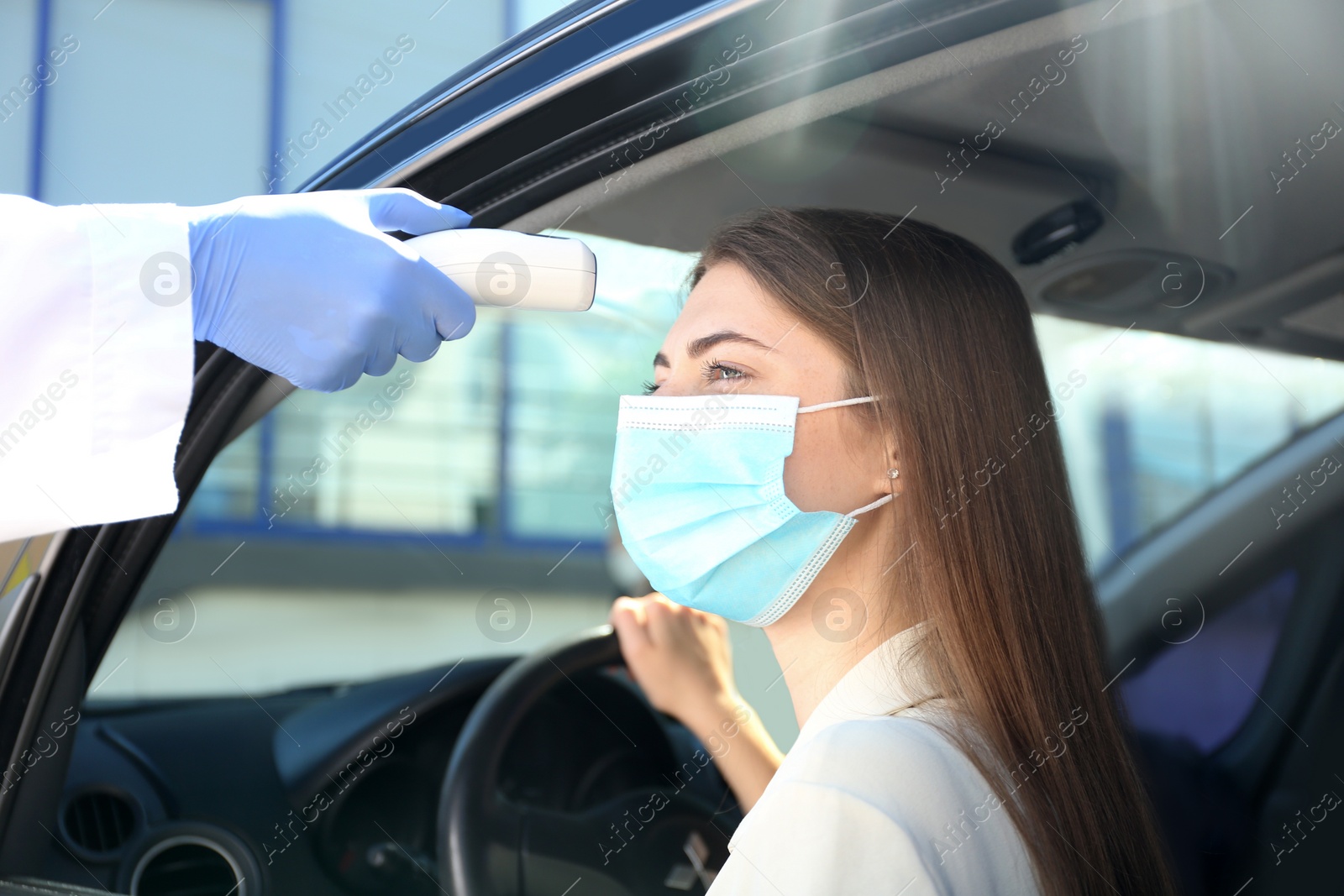 Photo of Doctor measuring woman's temperature with non contact infrared thermometer in car