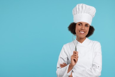 Photo of Happy female chef in uniform holding whisk on light blue background. Space for text