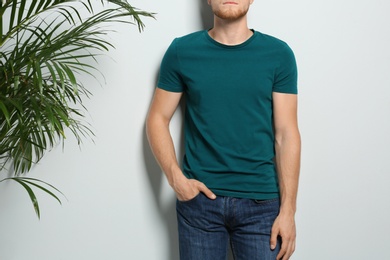 Photo of Young man wearing blank t-shirt on light background, closeup. Mockup for design