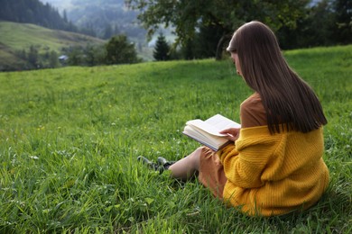 Photo of Young woman reading book on green meadow, back view