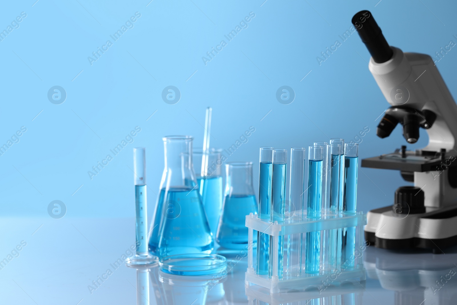 Photo of Microscope near different laboratory glassware and test tubes with light blue liquid on table