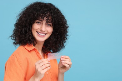 Photo of Young woman holding teeth whitening strips on light blue background, space for text