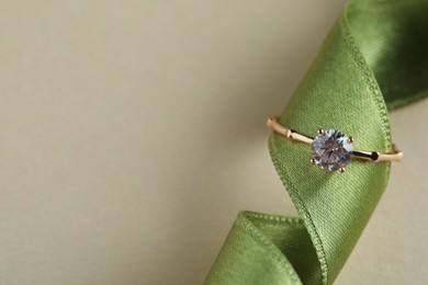 Photo of Beautiful engagement ring with gemstone on green ribbon against beige background, top view. Space for text
