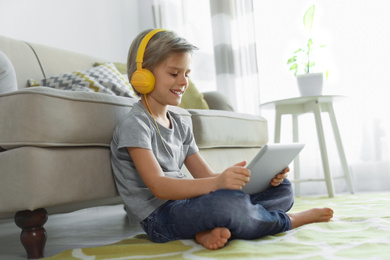 Photo of Cute little boy with headphones and tablet listening to audiobook at home