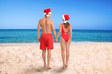 Image of Lovely couple with Santa hats on beach near sea, back view. Christmas vacation
