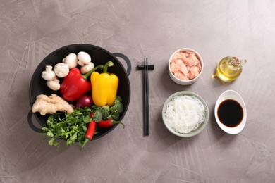 Photo of Wok, chopsticks and different products on grey textured table, flat lay