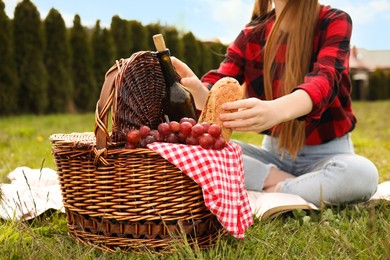 Photo of Girl taking bread from wicker picnic basket outdoors, closeup