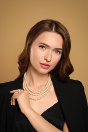 Photo of Young woman wearing elegant pearl jewelry on brown background
