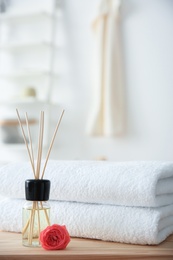 Photo of Reed air freshener and stack of towels on table against blurred background
