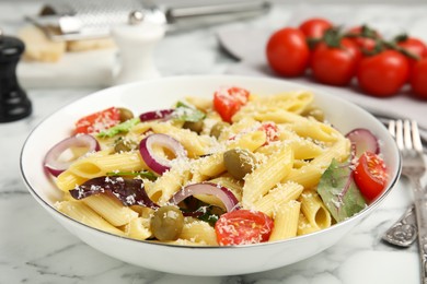 Photo of Bowl of delicious pasta with tomatoes, olives and onion on white marble table, closeup