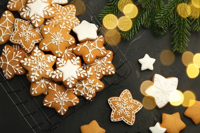 Photo of Tasty Christmas cookies with icing and fir tree branches on black table, flat lay