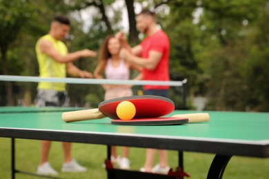 Photo of Friends talking near ping pong table outdoors, focus on rackets and ball