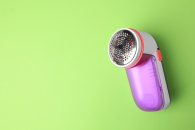Photo of Modern fabric shaver on light green background, top view. Space for text