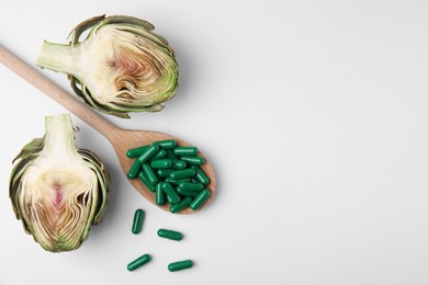 Photo of Spoon with pills and fresh artichoke on white background, flat lay. Space for text