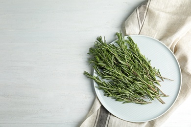 Photo of Plate with fresh rosemary twigs on wooden table, top view. Space for text