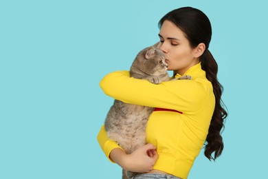 Photo of Young woman kissing her adorable cat on light blue background, space for text