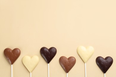 Photo of Different chocolate heart shaped lollipops on beige background, flat lay. Space for text