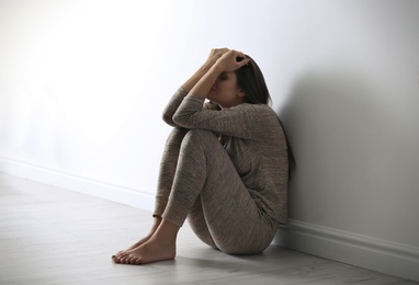 Photo of Depressed young woman sitting on floor near light wall
