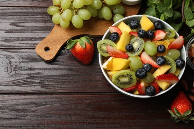 Photo of Tasty fruit salad in bowl and ingredients on wooden table, flat lay. Space for text