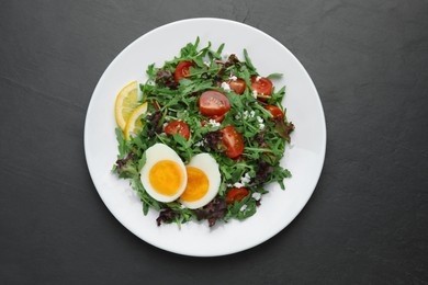 Photo of Delicious salad with boiled egg, arugula and tomatoes on black table, top view