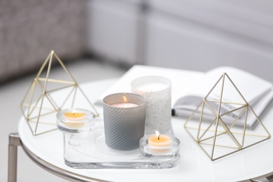 Photo of Burning candles in beautiful holders on white table indoors