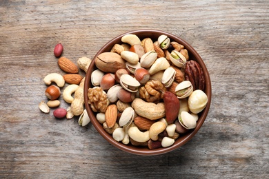 Photo of Bowl with mixed organic nuts on wooden background, top view