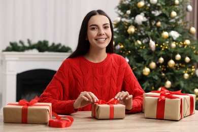 Photo of Happy woman decorating Christmas gift box at wooden table in room