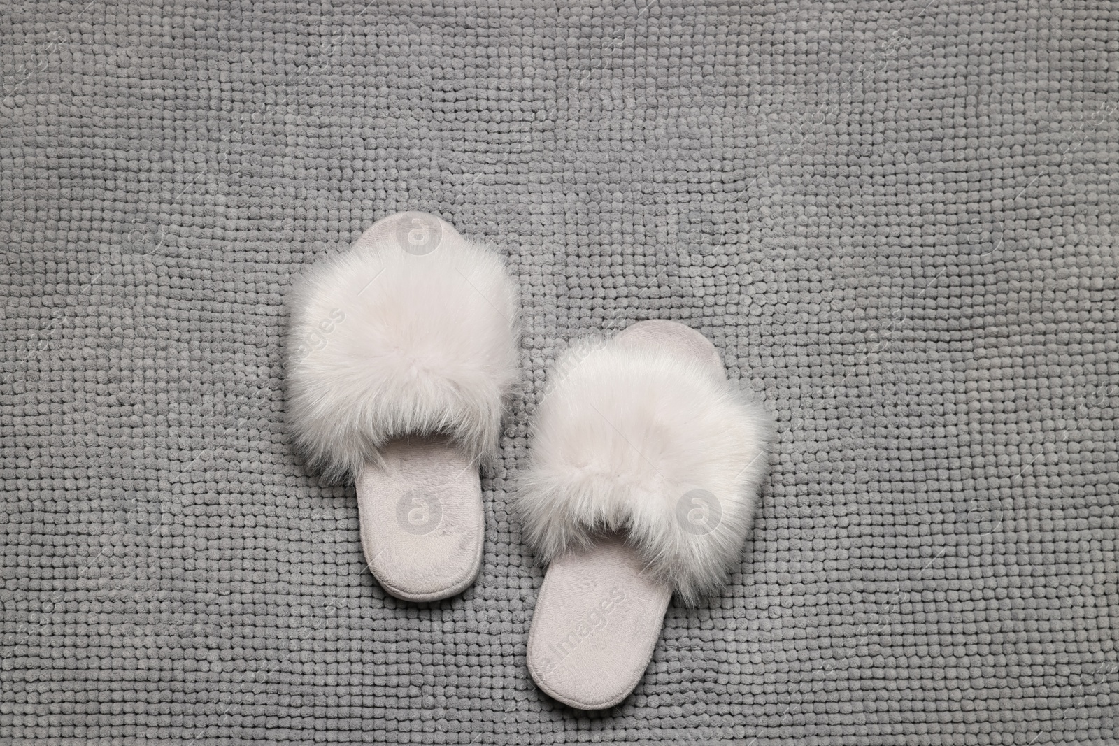 Photo of Slippers on soft grey bath mat, flat lay