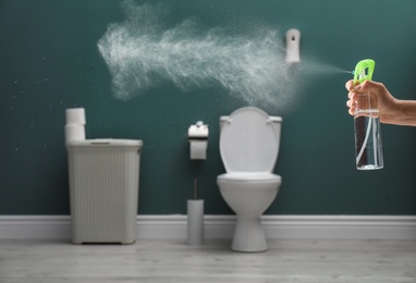 Photo of Woman spraying air freshener in bathroom