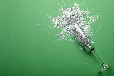 Photo of Glass and shiny confetti on green background, flat lay. Space for text