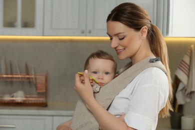 Photo of Mother feeding her cute child in sling (baby carrier) at home